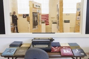 Yearbooks and typewriters sit in front of a window overlooking another room of the museum. 